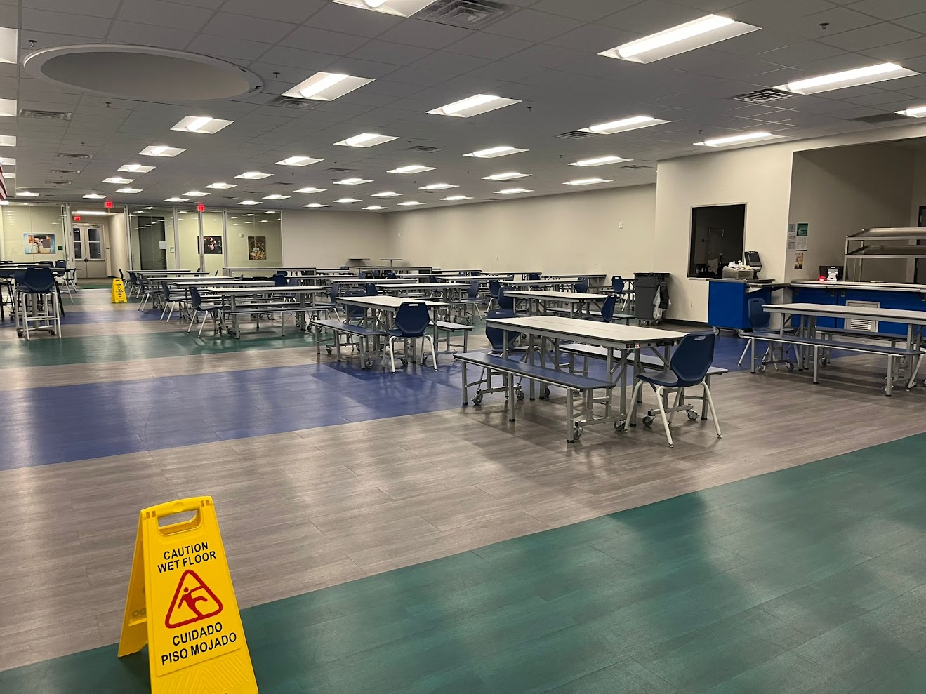 Clean school cafeteria with bilingual wet floor safety signage showing professional facility management